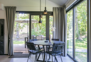 Salle à manger moderne avec grandes fenêtres et vue sur la forêt à Forest Park 't Wolfsven 15, Pays-Bas.