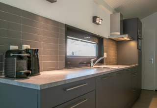 Modern kitchen with grey cabinets, window, coffee machine, and kettle at Forest Park ’t Wolfsven 15, Netherlands.