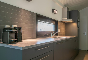 Cocina moderna con armarios grises, ventana, cafetera y hervidor en Forest Park ’t Wolfsven 15, Países Bajos.