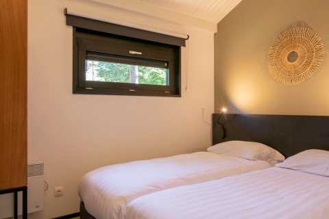 Schlafzimmer mit zwei Einzelbetten, weißer Bettwäsche und Fenster im Chalet Forest Park 't Wolfsven 15, Niederlande.
