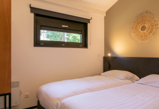 Bedroom with two single beds, white linens and a window at Forest Park 't Wolfsven 15 chalet in the Netherlands.