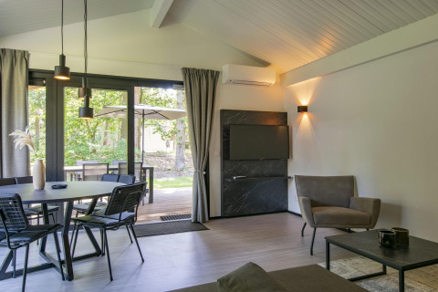 Salon moderne du chalet Forest Park 't Wolfsven 15 aux Pays-Bas, avec salle à manger et vue sur forêt.