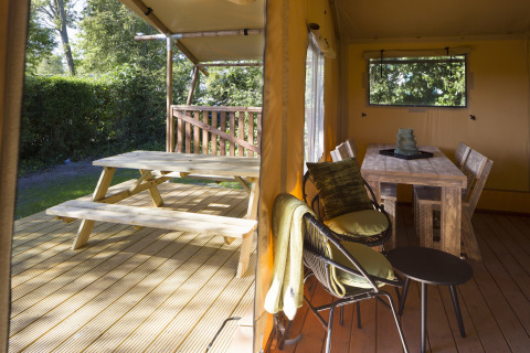 Blick auf Holzterrasse mit Picknicktisch und Essbereich in einem luxuriösen Safari-Zeltcamp.