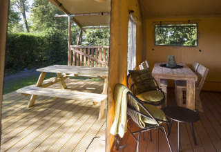 Udsigt over træterrasse med picnicbord og indretning af spiseområde i en safariteltslejr.