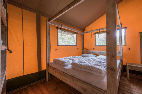 Dormitorio dentro de la tienda safari Forest Park 't Wolfsven 13 con cama doble y estructura de madera en Países Bajos.