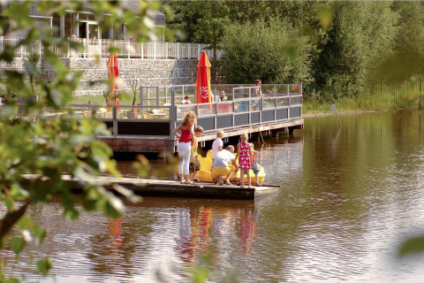 Familia sobre una balsa flotante en el lago, con café al aire libre y bosque en Forest Park 't Wolfsven.