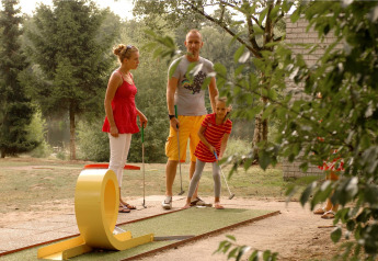 Une famille joue au mini-golf en plein air dans un parc verdoyant aux Pays-Bas, entourée d’arbres.
