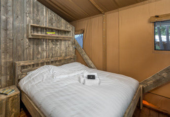 Chambre sous tente safari au Forest Park 't Wolfsven 12, Pays-Bas, avec lit en bois rustique et fenêtre.