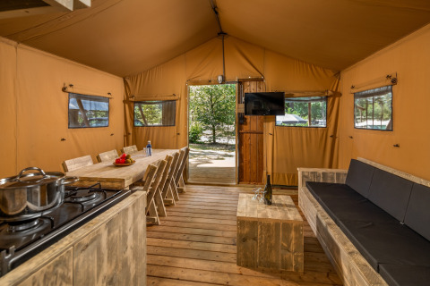 Vue intérieure de la tente safari Forest Park 't Wolfsven 12 aux Pays-Bas avec canapé et table à manger.