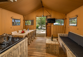 Vue intérieure de la tente safari Forest Park 't Wolfsven 12 aux Pays-Bas avec canapé et table à manger.