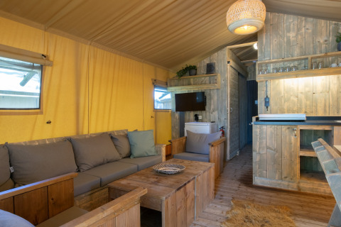 Cozy safari tent interior with wooden furniture and yellow canvas at Holiday Park Klein Vink in the Netherlands.