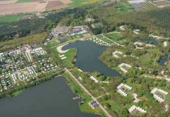 Vue aérienne d’un parc de vacances avec tentes safari, lacs, espaces boisés et champs ouverts en campagne.