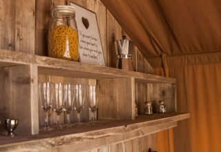 Træhylde i en safaritelts køkken med glas, pastaglas, kaffemaskine og krydderier på Holiday Park Klein Vink 21.