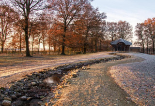 Photo of a safari tent at Holiday Park Klein Vink, Netherlands, with autumn trees and a small stream.