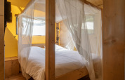 Bed with mosquito net in a safari tent at Holiday Park 'Klein Vink 19', Netherlands, with wood accents.