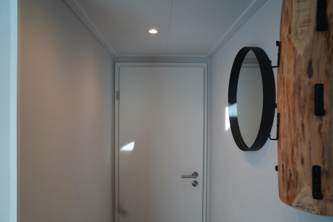 Corridoio minimalista in una tiny house con porta bianca, specchio rotondo e mensola in legno in Olanda.