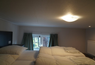 Bedroom in a tiny house at Holiday Park De Rimboe & De Woeste Hoogte 41 with low ceiling and cozy bedding.