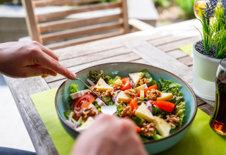 Persona che gusta un’insalata fresca con formaggio, noci e pomodori in una sistemazione glamping.