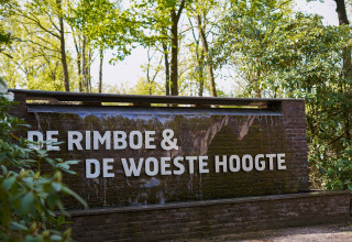 Bord bij de ingang van Holiday Park De Rimboe & De Woeste Hoogte 41, omgeven door bos in Nederland.
