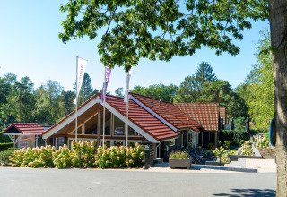 Glamping-Unterkunft mit rotem Ziegeldach, umgeben von Bäumen und Blumen an einem sonnigen Tag.