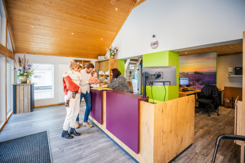 Une famille s'enregistre à la réception d'un hébergement glamping chaleureux au décor en bois moderne.