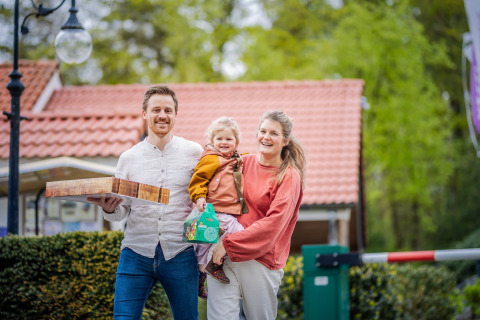 Famille souriante devant une tiny house au toit rouge au Holiday Park De Rimboe & De Woeste Hoogte, Pays-Bas.