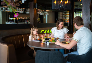 Famiglia che cena insieme in un ristorante moderno presso una struttura glamping, atmosfera accogliente.