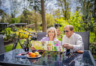 Älteres Paar sitzt an einem Tisch im Freien, studiert eine Karte bei Glamping-Unterkünften, Fahrräder im Hintergrund.