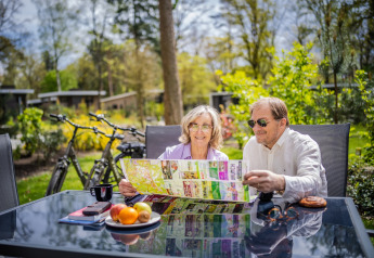 Couple âgé assis à une table extérieure, lit une carte dans un hébergement glamping, vélos en arrière-plan.