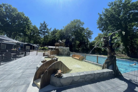 Piscine extérieure dans un site de glamping, entourée d’arbres et de décorations sous un ciel ensoleillé.
