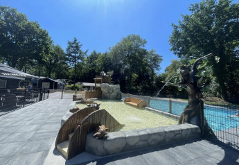 Outdoor pool area at a glamping site, surrounded by trees and whimsical decorations on a sunny day.