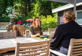 Zwei Frauen essen und unterhalten sich an einem Holztisch im Freien bei einer Glamping-Unterkunft.