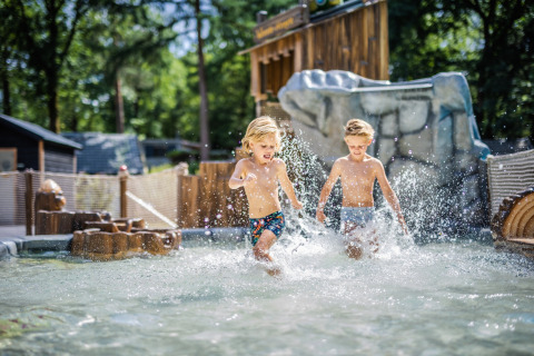 Two children splash and play in shallow water at a glamping site, enjoying a fun outdoor adventure.