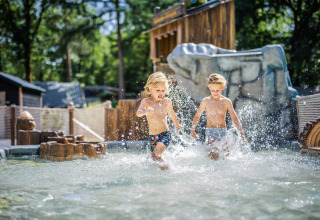 Deux enfants jouent et s’éclaboussent dans l’eau d’un hébergement glamping lors d’une journée ensoleillée.