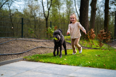Bambina che gioca con un cane nero con una palla nel parco Holiday Park De Rimboe & De Woeste Hoogte 41, Paesi Bassi.