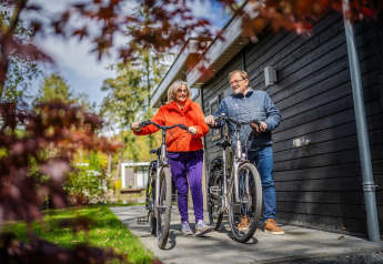 Senior couple with bicycles smiling in front of their modern glamping accommodation, enjoying nature.