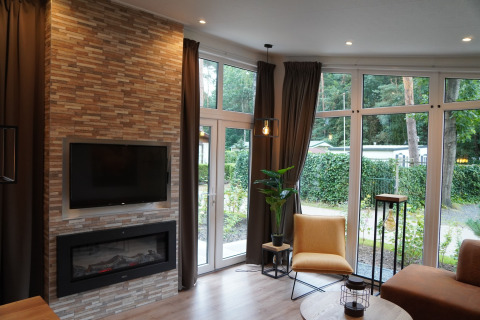 Intérieur de lodge moderne avec cheminée, TV, grandes fenêtres et vue sur jardin aux Pays-Bas.