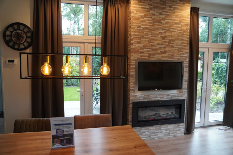 Sala en Holiday Park De Rimboe & De Woeste Hoogte 25 con chimenea, televisor y grandes ventanales.