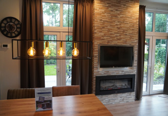 Living room at Holiday Park De Rimboe & De Woeste Hoogte 25 with fireplace, TV and large windows.