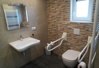 Baño accesible con barras de apoyo, lavabo, inodoro y ventana en Holiday Park De Rimboe, Países Bajos.