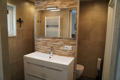 Baño moderno con lavabo blanco, espejo grande y azulejos beige en Holiday Park De Rimboe en Países Bajos.