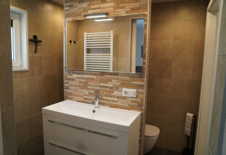 Modernes Badezimmer mit großem Spiegel, Waschbecken und beigen Fliesen in Holiday Park De Rimboe & De Woeste Hoogte.