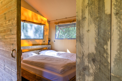 Cozy bedroom with double bed and rustic wood walls in a safari tent at Country Estate «Gerner 8», Netherlands.