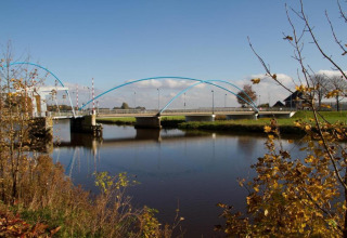 View of a modern bridge over a calm river near Country Estate Gerner 8, surrounded by autumn trees in the Netherlands.