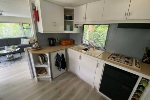 Moderne mobilhome-køkken i Sunhouse Bodhi, Holland, med hvide skabe, gaskomfur og udsigt til natur.