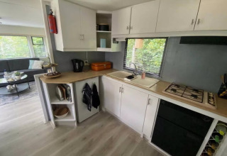 Moderne mobilhome-køkken i Sunhouse Bodhi, Holland, med hvide skabe, gaskomfur og udsigt til natur.