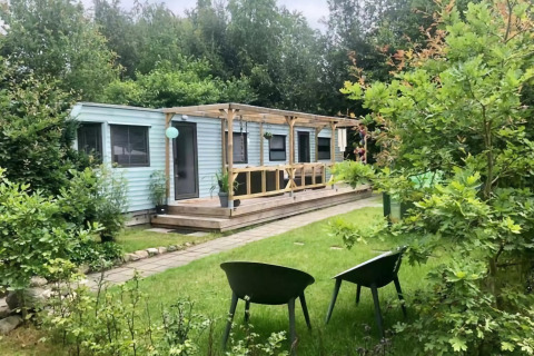 Mobilhjemmet Sunhouse Bodhi i Holland omgivet af grøn have og to stole foran verandaen.