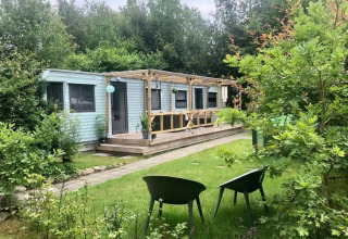 Mobilhjemmet Sunhouse Bodhi i Holland omgivet af grøn have og to stole foran verandaen.