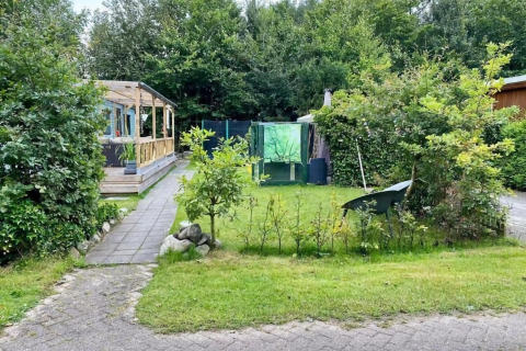 Mobilhjemmet Sunhouse Bodhi i Holland med grøn have, drivhus, træterrasse og omgivet af natur.
