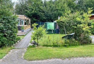 Mobilhjemmet Sunhouse Bodhi i Holland med grøn have, drivhus, træterrasse og omgivet af natur.